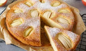 Ein goldbrauner Apfelkuchen, bestäubt mit Puderzucker, mit sichtbaren Apfelscheiben. Ein Stück ist herausgeschnitten. Ein gesunder Genuss!