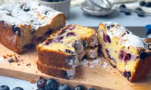 Saftiger skyrkuchen mit heidelbeeren, bestäubt mit Puderzucker. Frische Heidelbeeren liegen daneben.