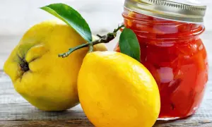 Gelbe Quittenfrucht und Zitrone neben einem Glas mit roter Marmelade.