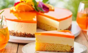 Erfrischende Aperol Torte mit Orangen-Gelee-Schicht und cremigem Käsekuchen. Ein Stück auf einem Teller mit Gabel.