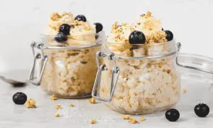 Zwei Gläser mit Overnight Oats, garniert mit Bananen, Blaubeeren und Granola. Perfekt für ein schnelles Frühstück.