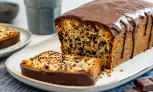 Ein saftiger Stracciatella Kuchen mit Schokoladenglasur, ein Stück davon auf einem Teller, daneben ein ganzer Kuchen.