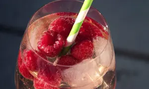 Erfrischender Pfirsich Spritz mit Himbeeren und Eiswürfeln in einem Glas, bereit zum Genießen.