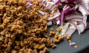 Gebratenes Hackfleischersatz-Granulat neben roten Zwiebeln in einer Pfanne.