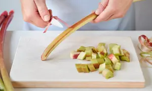 Hände schälen Rhabarber für das Kochen. Auf dem Brett liegen bereits geschnittene Stücke.