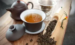 Dampfender Oolong Tee in einer Tasse, daneben eine Teekanne, ein Sieb und ein Löffel mit losem Tee. Die Oolong Tee Wirkung kann belebend sein.