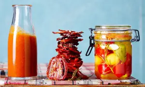Glas mit eingelegten Tomaten, daneben ein Stapel sonnengetrockneter Tomaten und eine Flasche Tomatensauce.