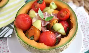 Erfrischender **Salat mit Melone**, Tomaten und Schinken, serviert in einer ausgehöhlten Honigmelone. Ein leichter Genuss!