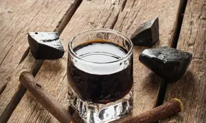 Ein Glas dunkler Flüssigkeit, umgeben von Lakritzstücken und -wurzeln. Perfekt für alle, die **Lakritz Schnaps selber machen** möchten.