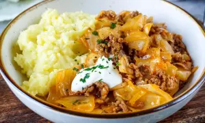 Herzhaftes Schmorkohl mit Hackfleisch, garniert mit einem Klecks Sour Cream und Petersilie, serviert mit cremigem Kartoffelpüree.
