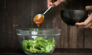 Ein Löffel mit köstlichem Salatdressing, wie im Restaurant, tropft auf frischen Salat in einer Glasschüssel.