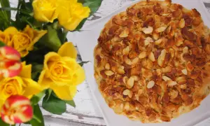 Bienenstich mandelkruste ohne backen, verziert mit gerösteten Mandelsplittern. Daneben ein Strauß gelber Rosen und Tulpen.