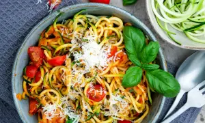 Herzhafte Zucchini-Nudeln mit Tomaten und Parmesan, garniert mit frischem Basilikum. Ein leichtes Gericht, das schmeckt.