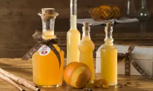 Flaschen mit selbstgemachtem Schnaps, Orangen, Zimtstangen und Sternanis auf Holztisch.