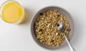 Schüssel mit dinkelflocken oder haferflocken, Nüssen und Trockenfrüchten, daneben ein Glas Orangensaft.