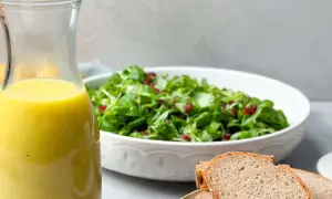 Ein Glas mit gelbem Dressing steht neben einem Salat und Brot. Perfekt für ein Kartoffel Dressing!