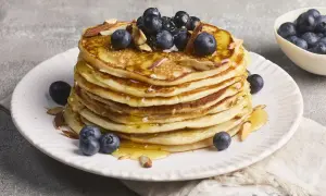 Stapel protein pancakes mit Magerquark, garniert mit Blaubeeren und Mandelsplittern, beträufelt mit Honig.