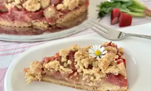 Ein saftiges Stück Rhabarberkuchen mit Schmand und Streuseln, garniert mit einer kleinen Gänseblümchen.