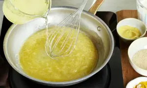 Flüssigkeit wird in eine Pfanne gegossen, während mit einem Schneebesen gerührt wird. Zutaten für eine vegane Sauce Hollandaise werden vorbereitet.