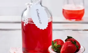 Flasche mit selbstgemachtem Erdbeersirup, garniert mit frischen Erdbeeren. Perfekt für Cocktails oder als Topping.