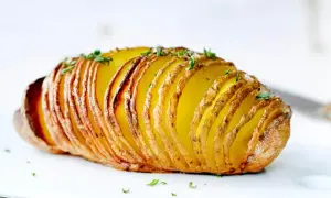Eine goldbraune Hasselback Kartoffel, knusprig und mit frischen Kräutern bestreut, wartet darauf, genossen zu werden.
