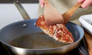 Ein saftiges Schweinefilet wird mit zwei Holzspateln in einer Pfanne gewendet, um es perfekt zu braten.