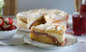 Ein saftiger Rhabarberkuchen mit Baiser, wie ihn Landfrauen backen. Ein Stück auf einem Teller, daneben frischer Rhabarber.
