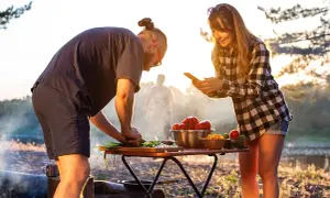 Ein Paar bereitet draußen Gemüse zu, während die Sonne untergeht. Sie kochen im Wohnmobil und genießen die Natur.