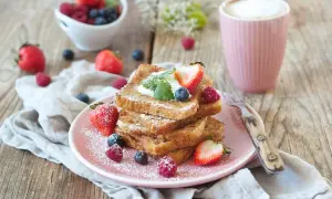 Ein Stapel goldbrauner French Toast, bestäubt mit Puderzucker, garniert mit Beeren und Sahne. Ein köstlicher Start in den Tag!