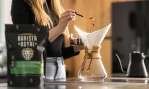 Frau gibt mit Löffel Kaffeepulver in den Filter, um Filterkaffee zu kochen. Daneben steht eine Packung Barista Royal Kaffee.