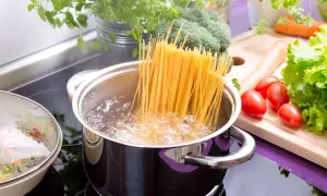 Spaghetti kochen in sprudelndem Wasser. Frisches Gemüse wie Brokkoli, Karotten und Tomaten liegen bereit für eine leckere Mahlzeit.