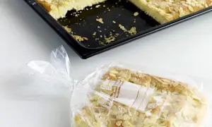 Ein Stück Mandelkuchen ist in einer Plastiktüte verpackt, bereit zum Kuchen einfrieren. Daneben liegt die Backform mit den restlichen Stücken.