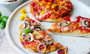 Zwei kleine Pizzen, eine mit Pilzen und Zwiebeln, die andere mit Mais und Paprika, warten darauf, aufgebacken zu werden.