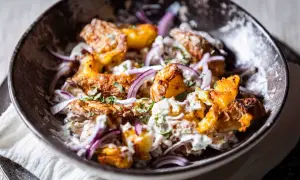 Knuspriger Kartoffelsalat mit cremiger Soße, roten Zwiebeln und frischer Petersilie in einer dunklen Schüssel.