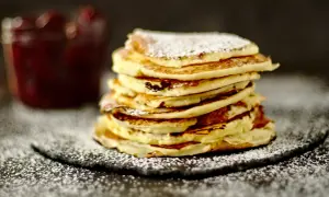 Ein Stapel fluffiger Quark Pfannkuchen, bestäubt mit Puderzucker, neben einem Glas Marmelade.