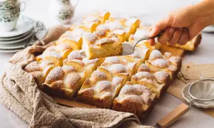 Ein Stück eines saftigen Blechkuchens mit Puderzucker wird herausgehoben. Perfekt für schnelle Blechkuchen Rezepte.