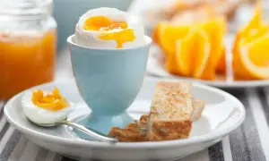 Ein perfekt gekochtes Ei im Wasserkocher, serviert mit Toast und Orangenspalten.