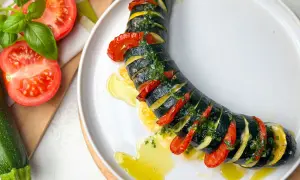 Zucchini Caprese: geschichtete Zucchini, Tomaten und Kräuter, beträufelt mit Olivenöl auf einem weißen Teller.
