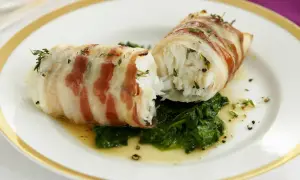 Zwei Fischröllchen, in Speck gewickelt, auf Spinatbett. Ein festliches Gericht, perfekt für Fischgerichte an Weihnachten.