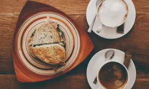 Ein Sandwich und zwei Kaffees auf einem Holztisch. Der Kaffee könnte mit Kaffeesirup verfeinert werden.