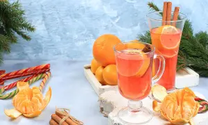Zwei Gläser mit einem heißen Aperol-Getränk, garniert mit Orangen und Zimt. Daneben Mandarinen, Zuckerstangen und Tannenzweige.