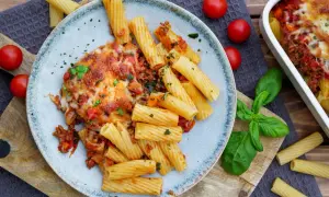 Herzhaftes Bolognese Gratin mit Rigatoni, überbacken mit geschmolzenem Käse, garniert mit frischem Basilikum und Tomaten.