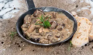 Herzhafte Champignon Rahmsauce in einer Pfanne, garniert mit Rosmarin, serviert mit knusprigem Brot.