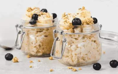 Zwei Gläser mit Overnight Oats, garniert mit Bananen, Blaubeeren und Granola. Perfekt für ein schnelles Frühstück.
