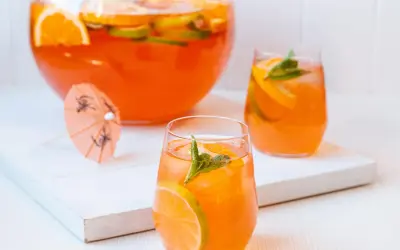 Erfrischende Aperol Bowle mit Orangen- und Limettenscheiben, garniert mit Minze. Perfekt für heiße Sommertage.