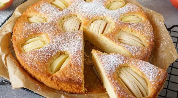 Ein goldbrauner Apfelkuchen, bestäubt mit Puderzucker, mit sichtbaren Apfelscheiben. Ein Stück ist herausgeschnitten. Ein gesunder Genuss!
