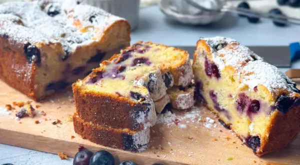 Saftiger skyrkuchen mit heidelbeeren, bestäubt mit Puderzucker. Frische Heidelbeeren liegen daneben.