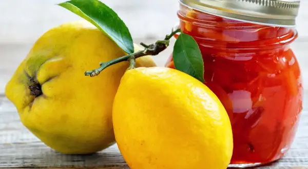 Gelbe Quittenfrucht und Zitrone neben einem Glas mit roter Marmelade.