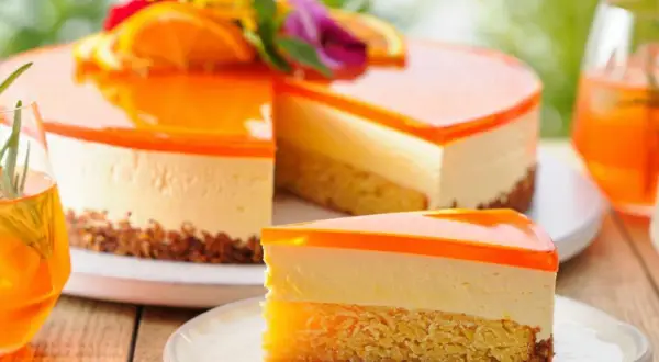 Erfrischende Aperol Torte mit Orangen-Gelee-Schicht und cremigem Käsekuchen. Ein Stück auf einem Teller mit Gabel.