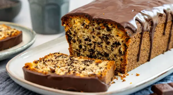Ein saftiger Stracciatella Kuchen mit Schokoladenglasur, ein Stück davon auf einem Teller, daneben ein ganzer Kuchen.